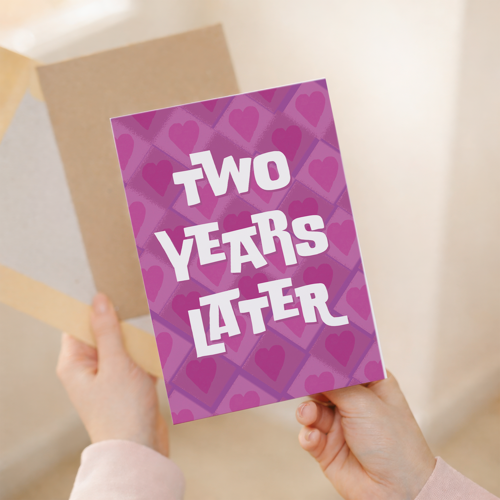 A simple and modern 2nd wedding anniversary greeting card featuring a large number 2 in pink, white, and purple floral patterns on eco-friendly cardstock, paired with a brown Kraft envelope.