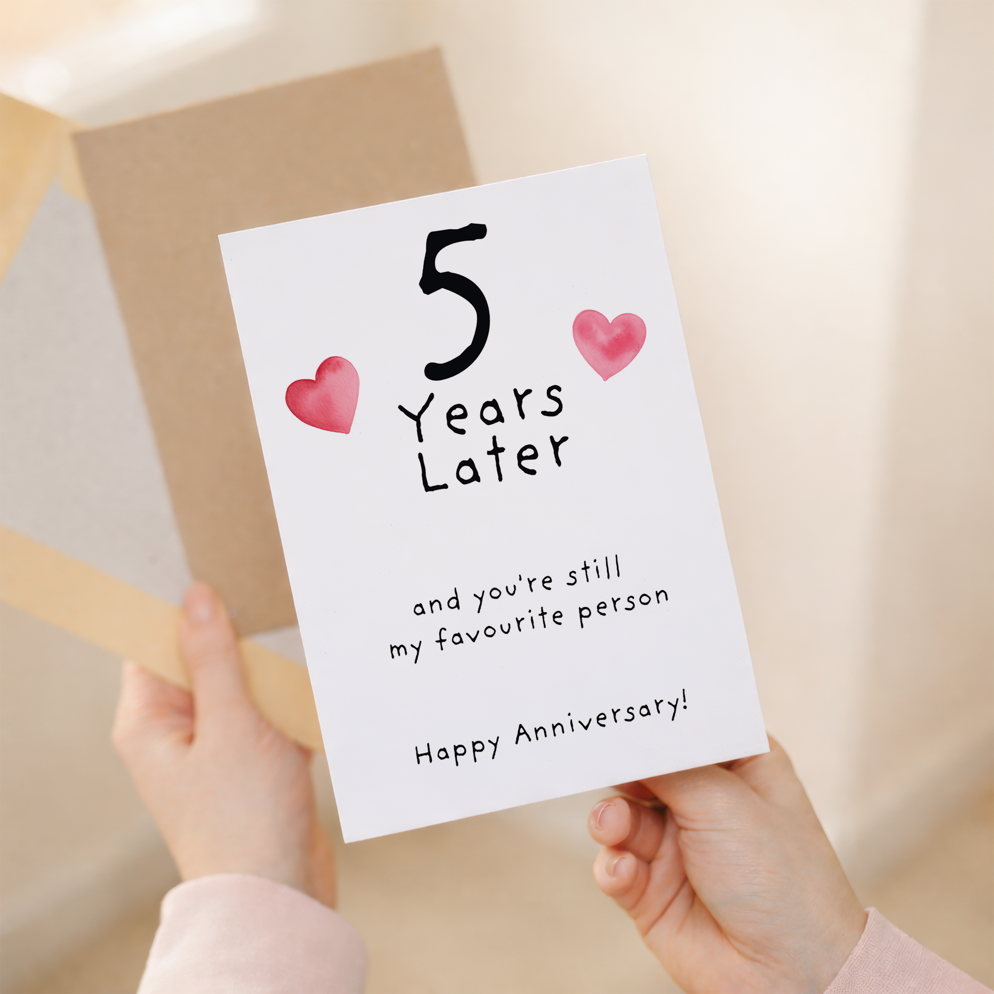 Elegant 5th wedding anniversary greeting card featuring a large number five decorated with blue floral patterns, paired with a brown kraft envelope on a wooden background.