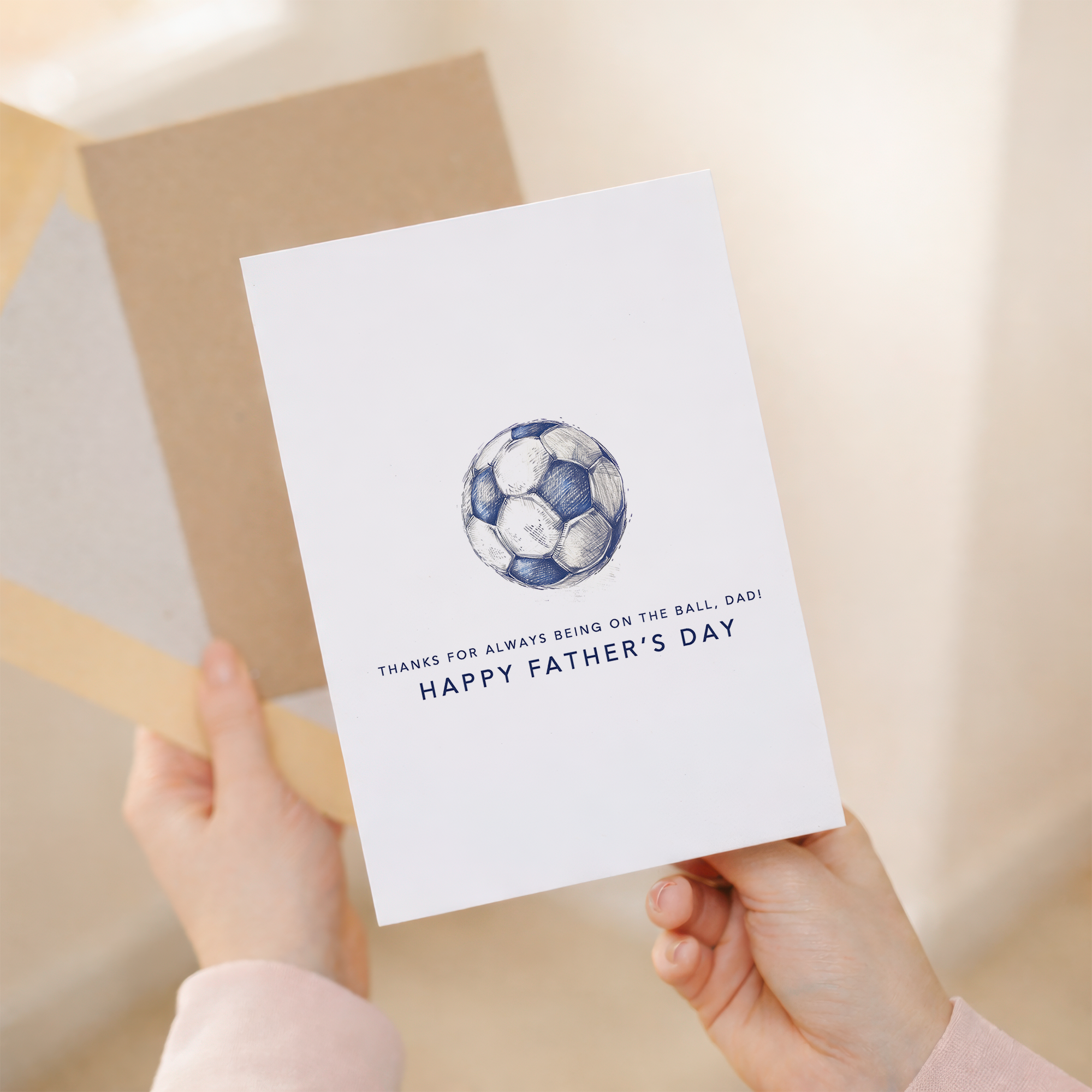 Minimalist Father's Day greeting card featuring a blue and white football with the text "On the ball Dad" on a white background.