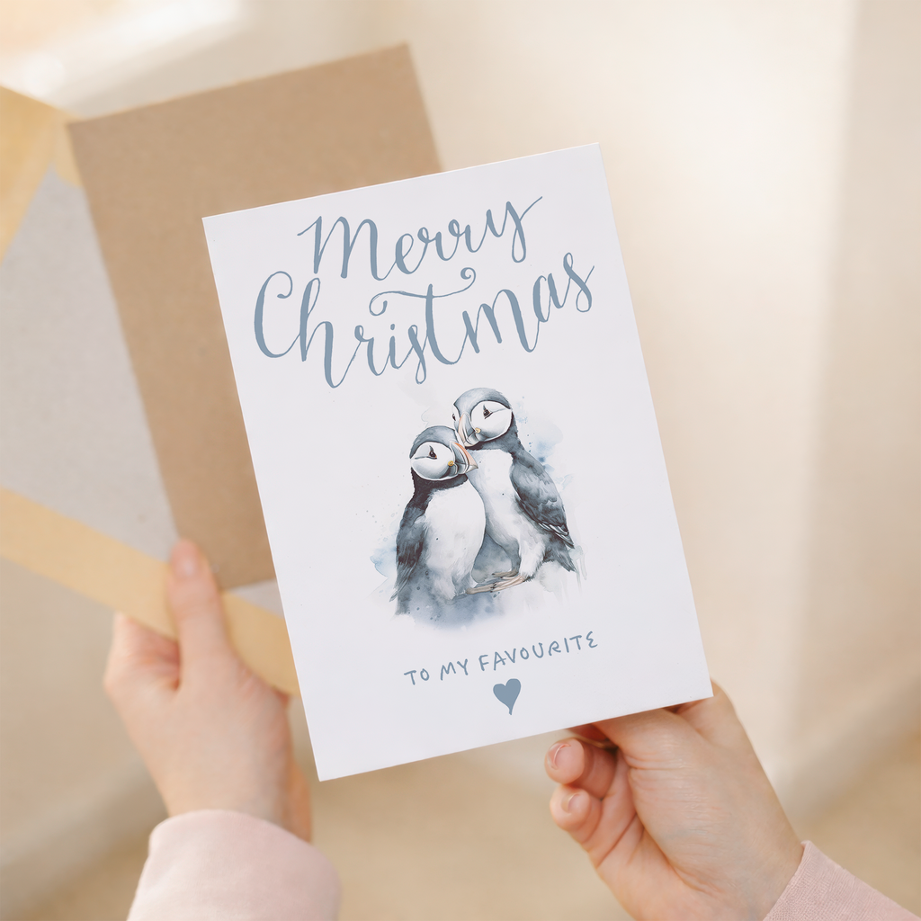 A festive Christmas greeting card featuring a cute illustration of two puffins.