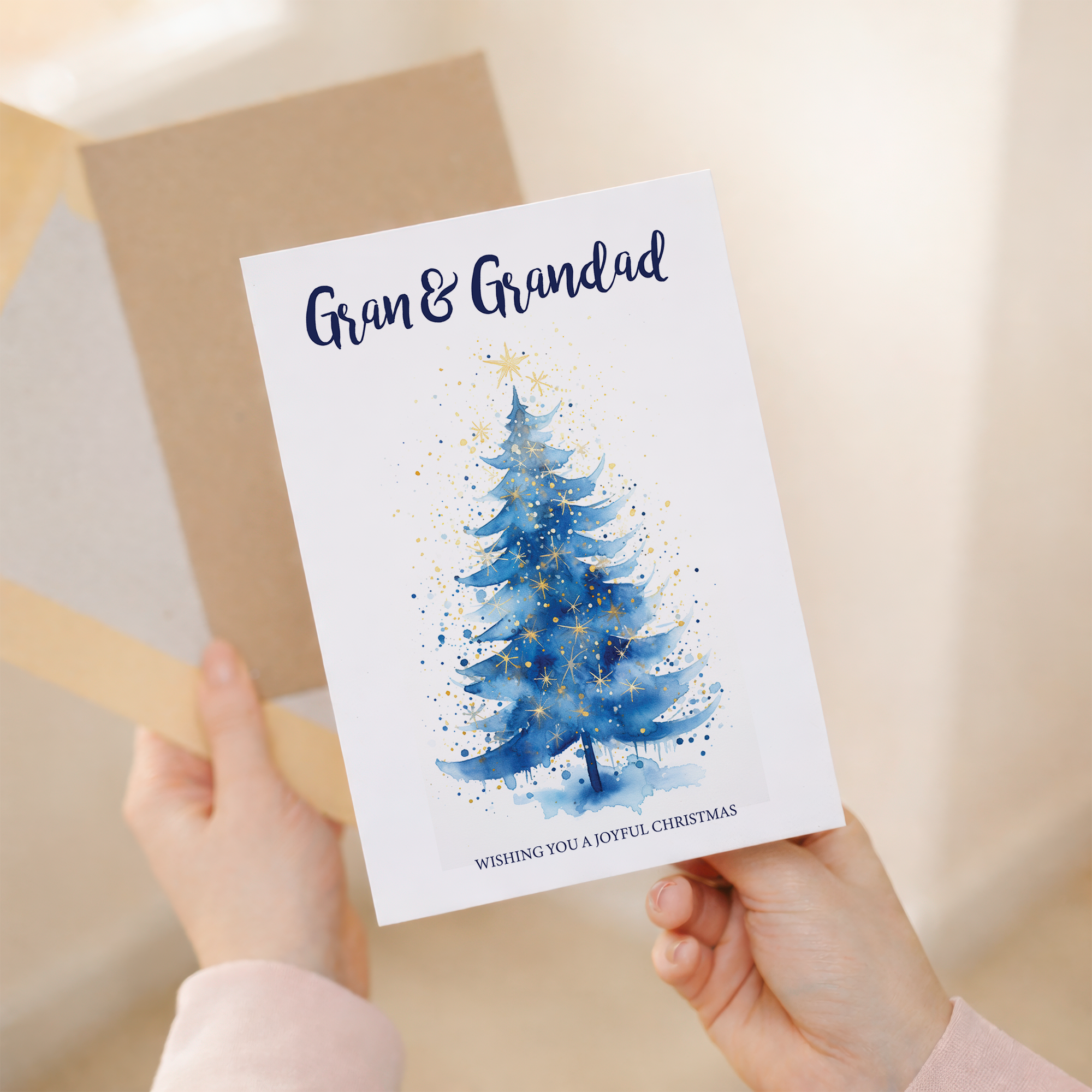 A festive Christmas greeting card featuring a decorated green Christmas tree with a gold star on top, set against a clean white background with a brown kraft envelope.