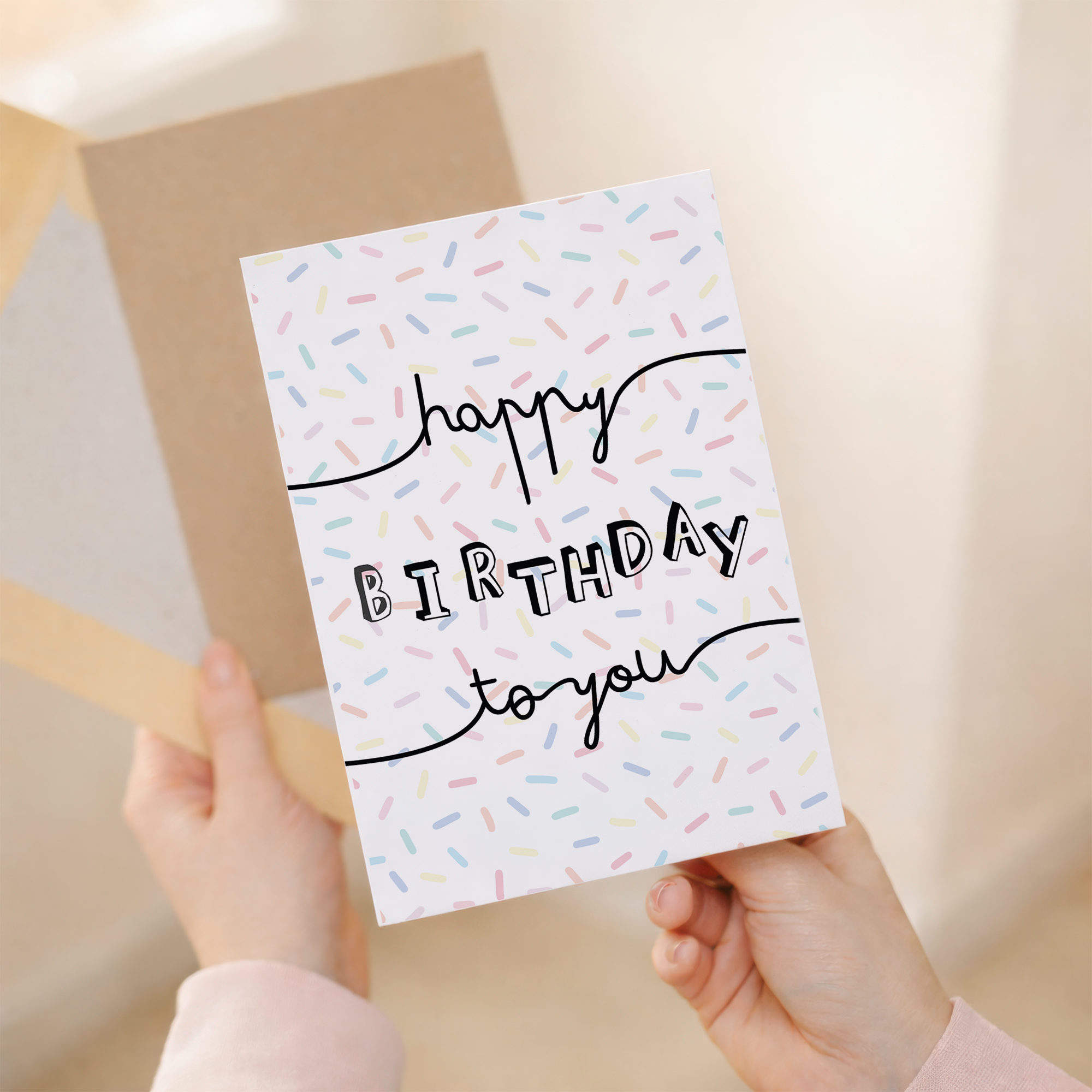 A stylish birthday greeting card featuring a typographic letters and numbers design on sustainable recycled cardstock, paired with a brown Kraft envelope.