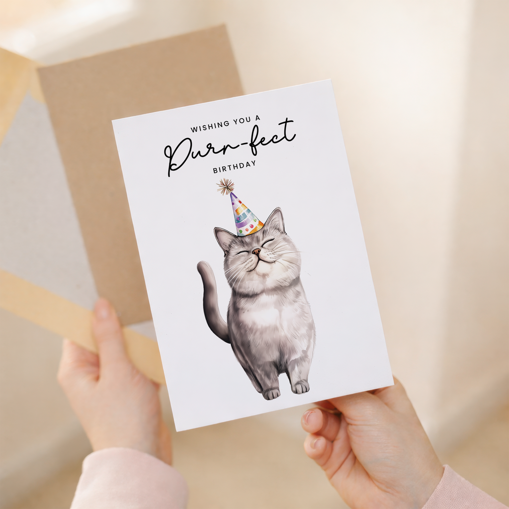 A portrait-oriented birthday card featuring an illustration of a grey British Shorthair cat wearing a colorful party hat, set against a plain background with the message "Wishing You a Purr-fect Birthday."
