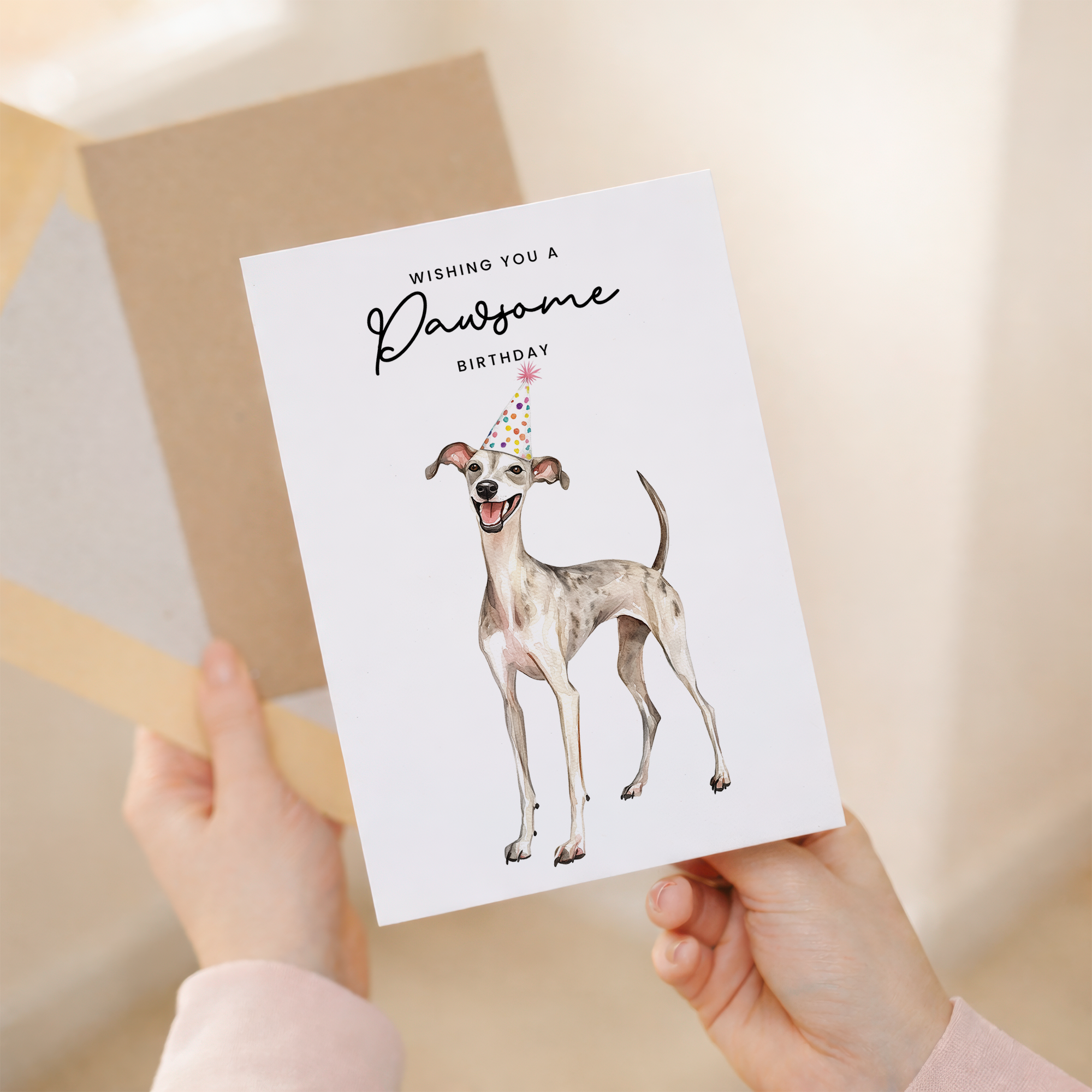 A watercolor illustration of a whippet wearing a colorful party hat on a white greeting card.