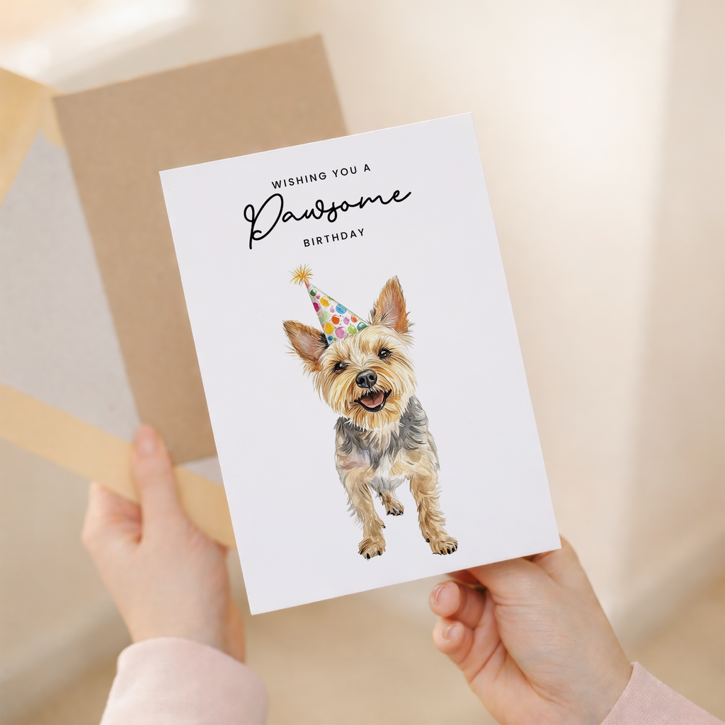 A cute Yorkshire Terrier wearing a colorful party hat on a white background with the text Wishing You a Pawsome Birthday.