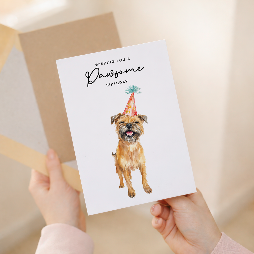 A cute Border Terrier wearing a colorful party hat on a minimalist birthday greeting card with the text Wishing You a Pawsome Birthday.