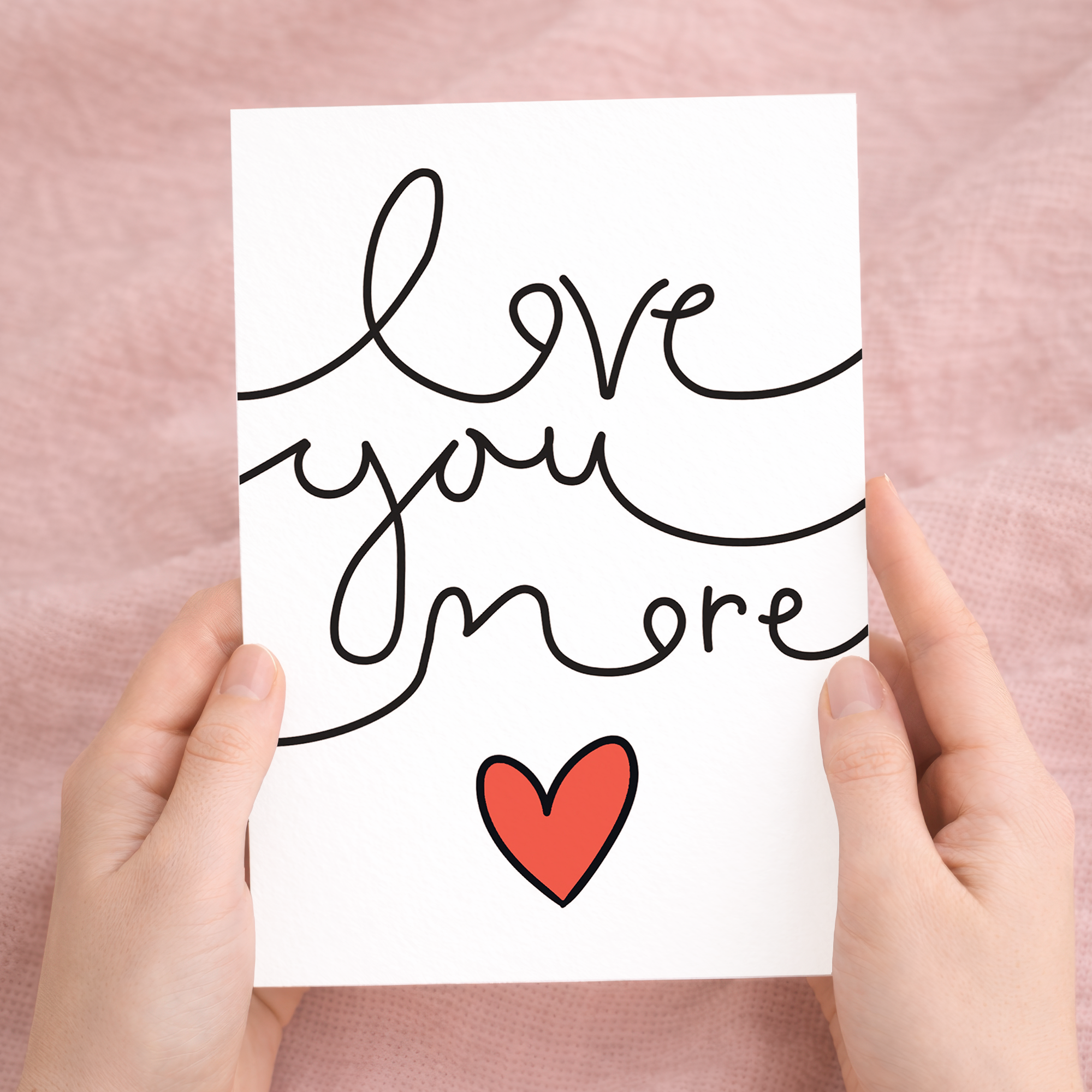 Minimalist Valentine's Day greeting card featuring the text Love You More in a stylish script on sustainable recycled cardstock, accompanied by a brown Kraft envelope.