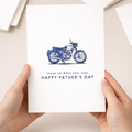 A simple and modern Father's Day greeting card for motorcycle enthusiasts featuring a minimalist blue motorbike illustration and the punny text You're the Wheel Deal Dad on a white background.