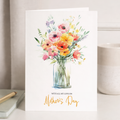 A Mother's Day greeting card featuring a vibrant floral design with pink, yellow, and orange flowers on a white background.
