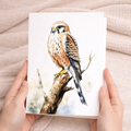 A detailed watercolor painting of a kestrel bird perched on a branch, featured on a vertical greeting card.