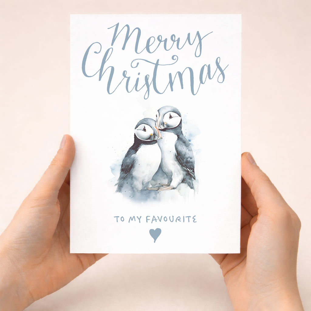 A festive Christmas greeting card featuring a cute illustration of two puffins.
