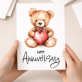 Cute teddy bear holding a large red love heart anniversary greeting card for a wife, husband, boyfriend, or girlfriend.