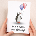 Cute illustrated birthday card for children featuring a happy puffin bird with a colorful party hat on a plain background.