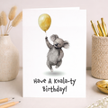 A cute koala illustration on a birthday card for children, featuring a soft gray koala with large ears and a gentle expression.