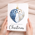 A romantic Christmas greeting card featuring a charming illustration of two owls perched inside a decorative holiday bauble with a red love heart.