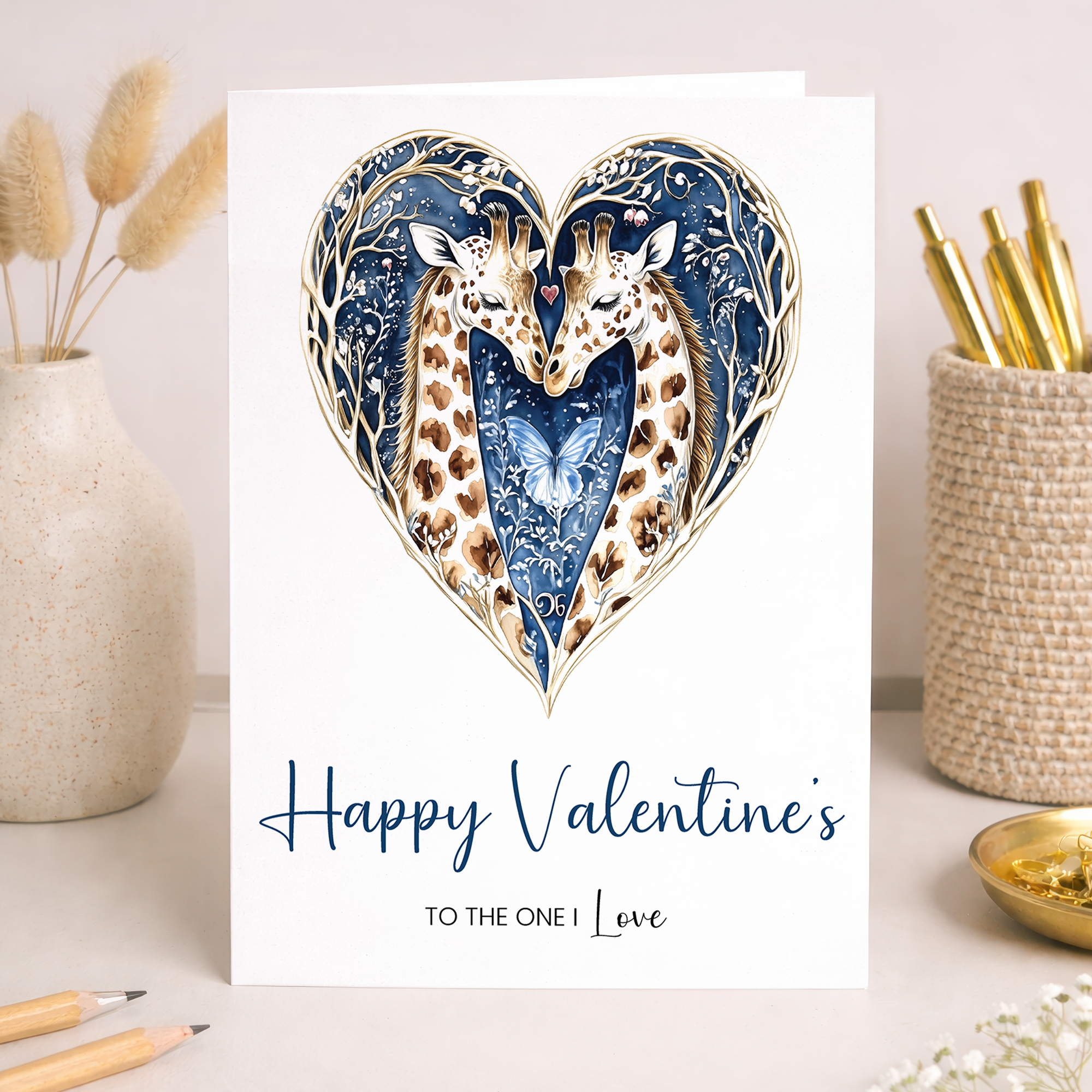 A romantic Valentine's Day card featuring an illustration of two giraffes whose necks curve together to form a heart shape, placed on top of a brown kraft envelope.