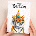 A vibrant watercolor illustration of a tiger's face on a white greeting card with modern, artistic detailing.
