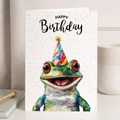 A watercolor illustration of a cute green frog on a white birthday card.