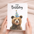 A charming watercolor illustration of a brown bear on a white birthday greeting card.