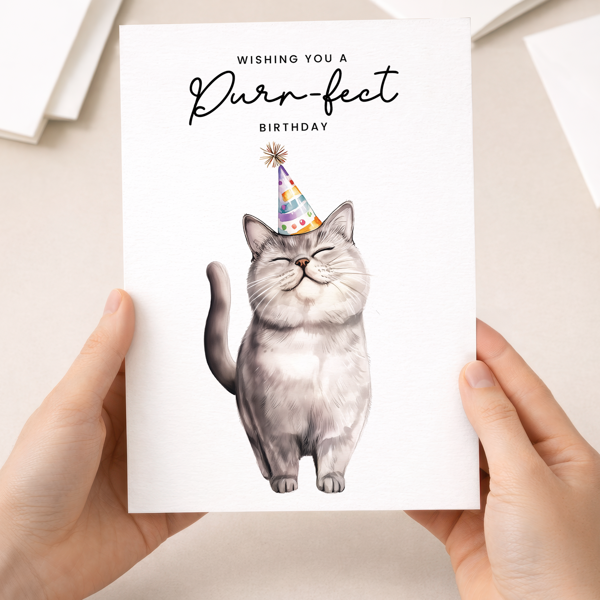 A portrait-oriented birthday card featuring an illustration of a grey British Shorthair cat wearing a colorful party hat, set against a plain background with the message "Wishing You a Purr-fect Birthday."