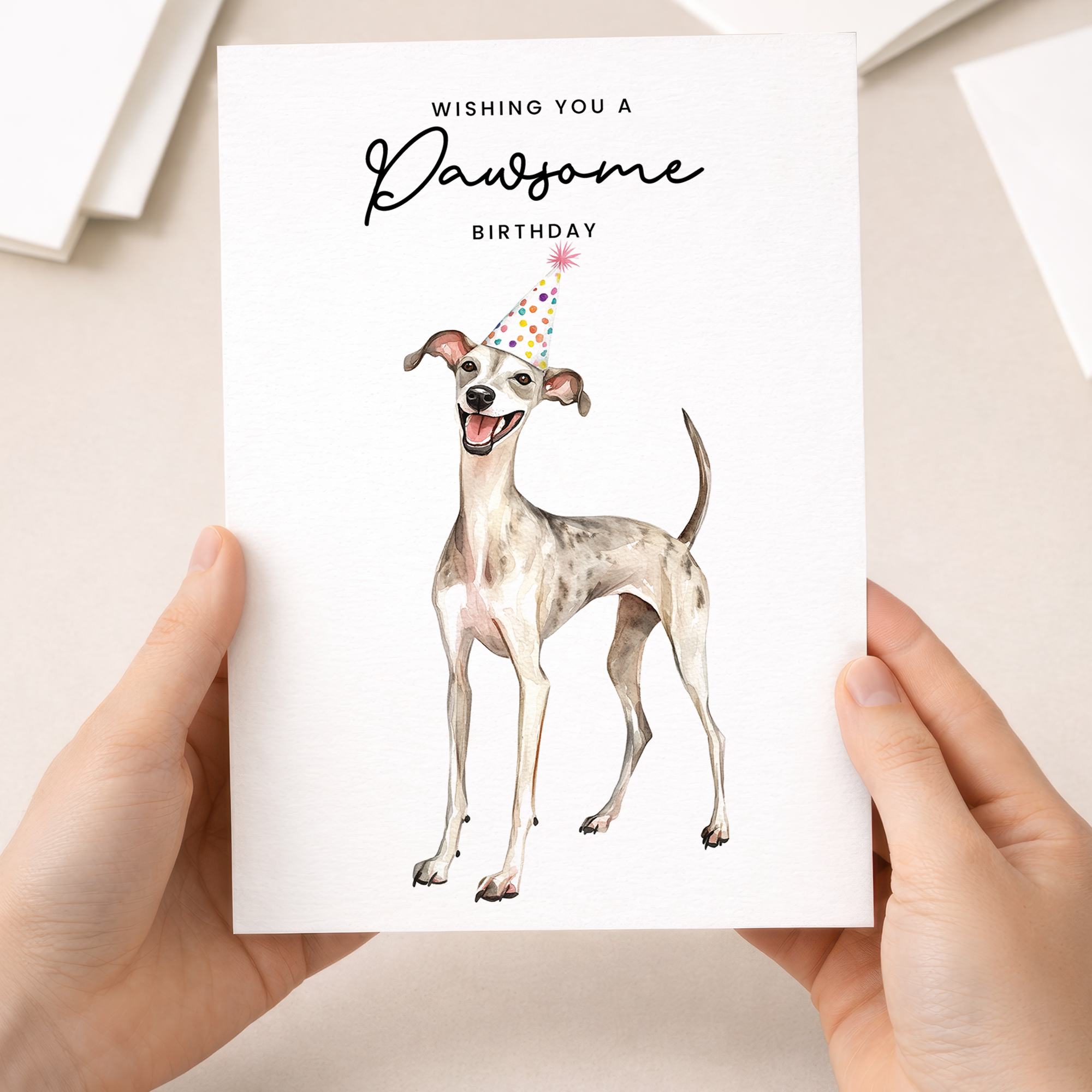 A watercolor illustration of a whippet wearing a colorful party hat on a white greeting card.