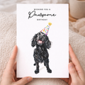 A portrait-oriented greeting card featuring an illustration of a Cocker Spaniel wearing a colorful party hat with the caption Wishing You a Pawsome Birthday.