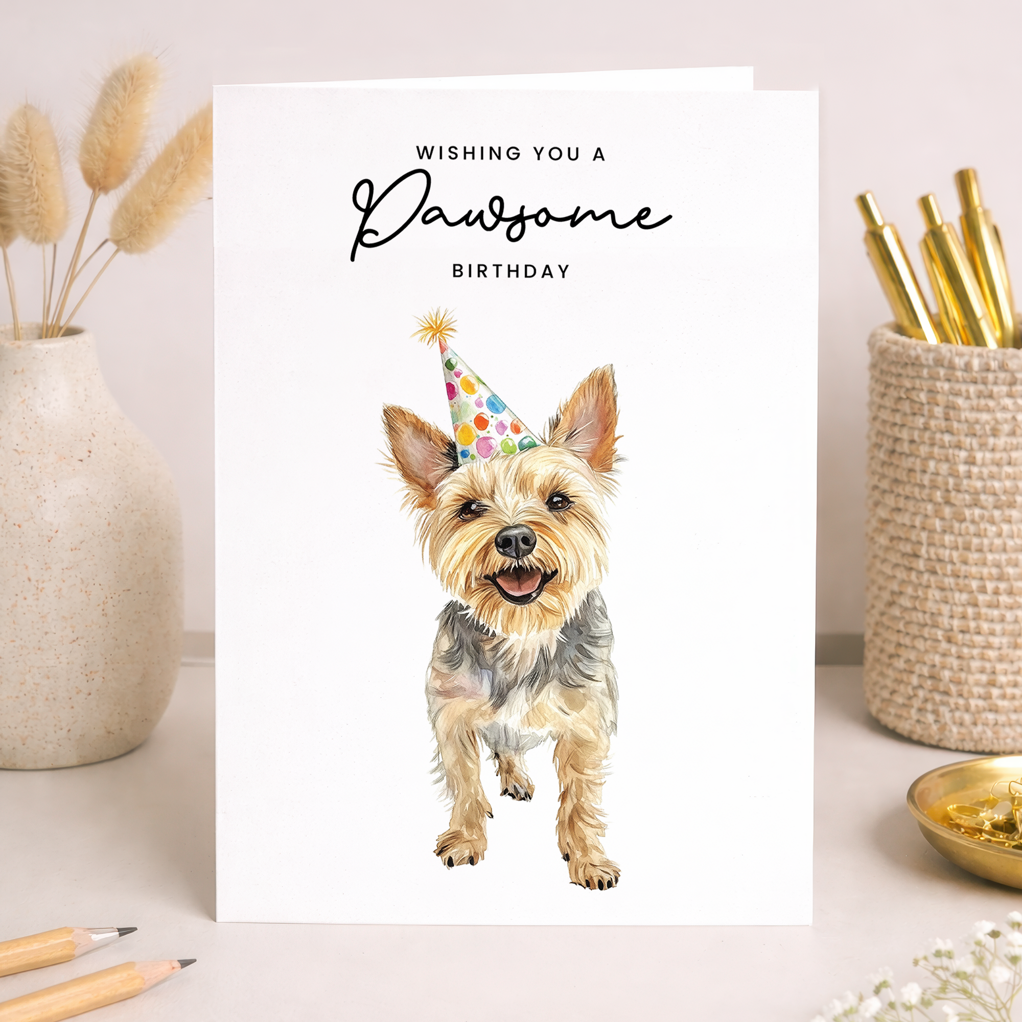 A cute Yorkshire Terrier wearing a colorful party hat on a white background with the text Wishing You a Pawsome Birthday.