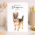 German Shepherd puppy wearing a colorful party hat surrounded by paw prints on a minimalist birthday greeting card.